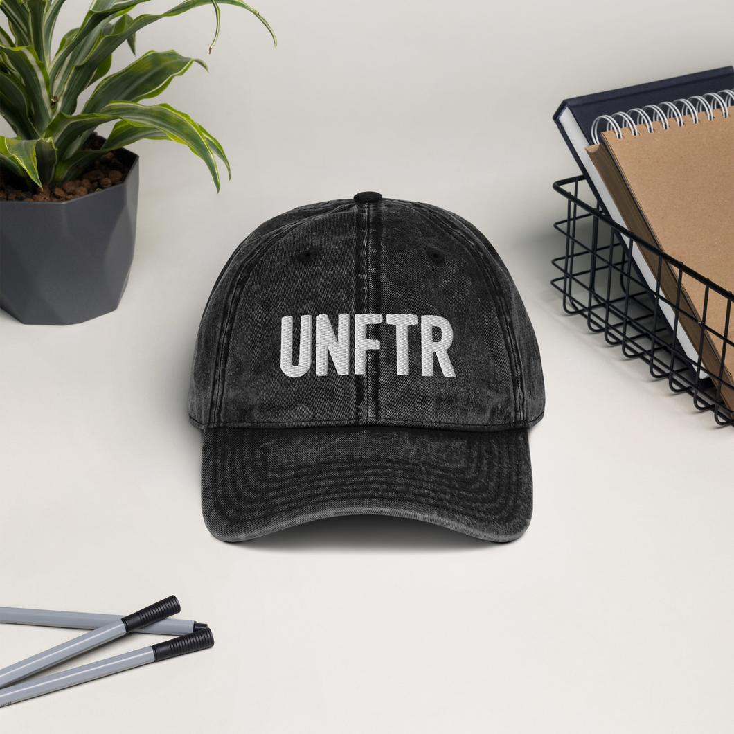 Black/Grey vintage wash dad cap with white UNFTR logo embroidered on the front.